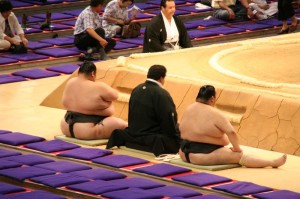 Un des arbitres au bord du dohyo, entouré de deux lutteurs de bonne envergure